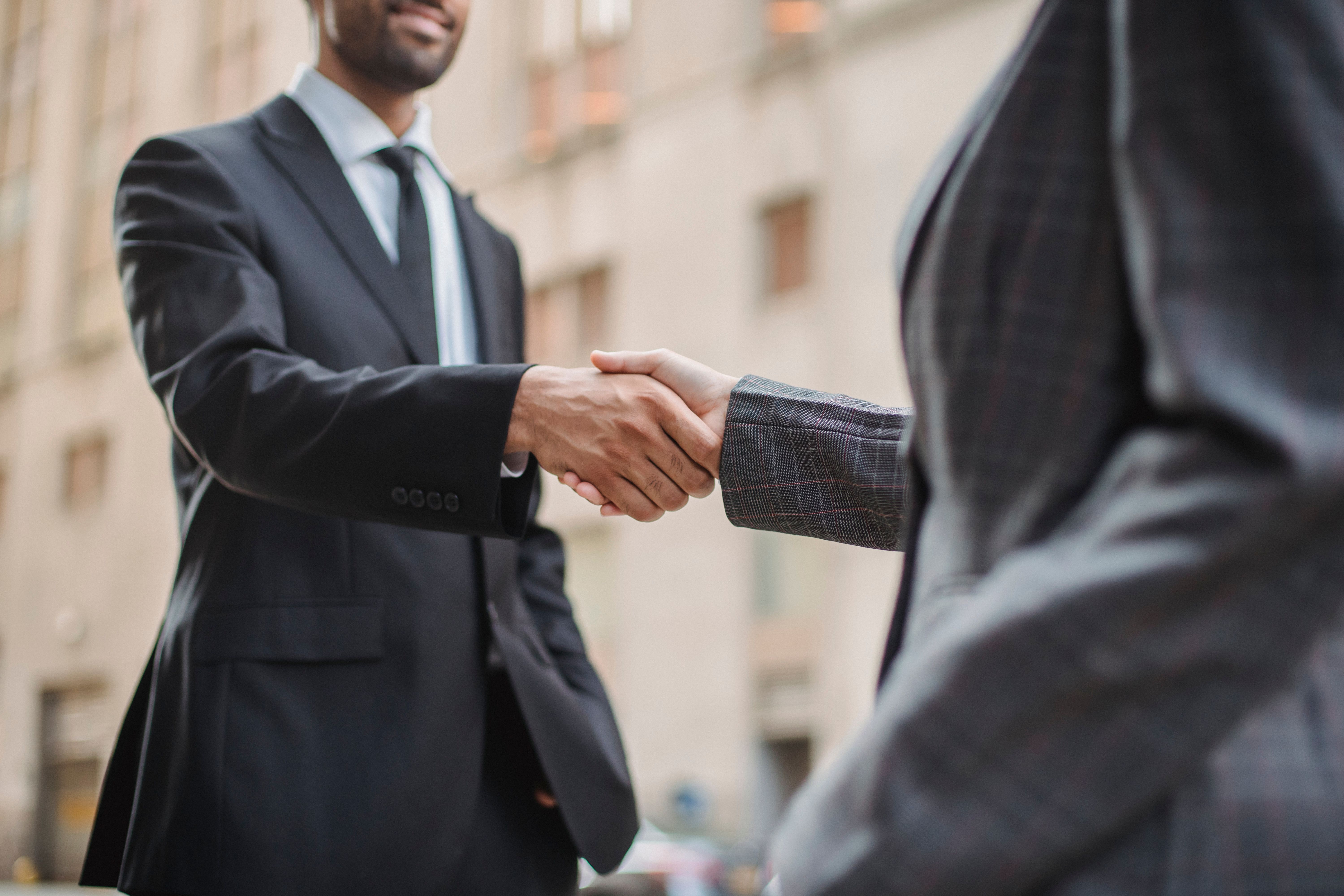 Two professionals shaking hands over a meeting table with analytics data on screen